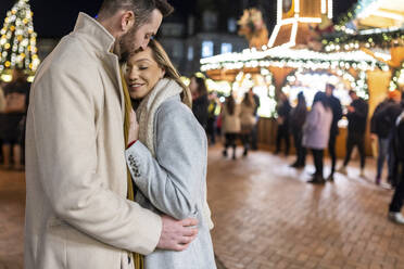 Glückliches Paar umarmt sich auf dem Weihnachtsmarkt - WPEF07359