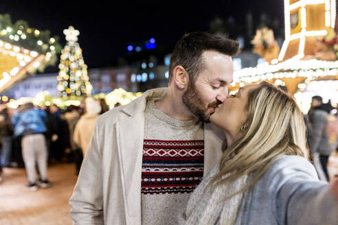 Junge Frau und Mann küssen sich auf dem Weihnachtsmarkt - WPEF07362
