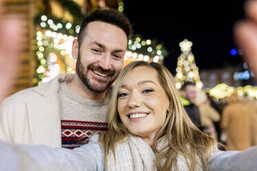 Ein fröhliches Paar, das seine Erinnerungen an einen festlichen Weihnachtsmarkt mit einem fröhlichen Selfie festhält - WPEF07363