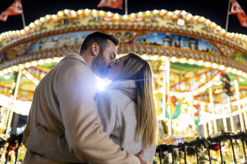 Sich küssendes Paar vor einem Karussell auf dem Weihnachtsmarkt - WPEF07368