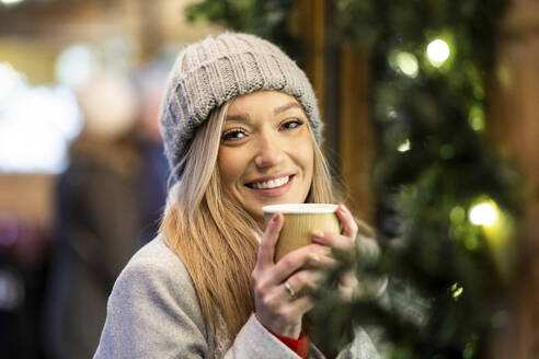 Lächelnde junge Frau mit Kaffeetasse auf dem Weihnachtsmarkt - WPEF07384