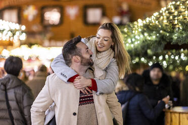 Glücklicher Mann, der eine Frau auf dem Weihnachtsmarkt huckepack nimmt - WPEF07386