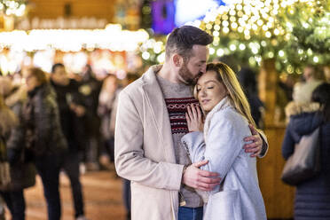 Mann küsst und umarmt Frau auf dem Weihnachtsmarkt - WPEF07387