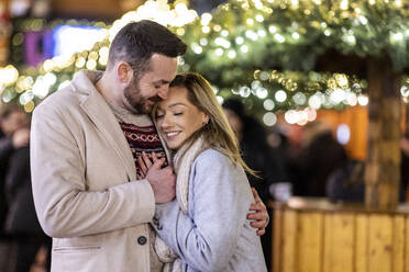 Glückliches Liebespaar, das sich auf dem Weihnachtsmarkt umarmt - WPEF07388