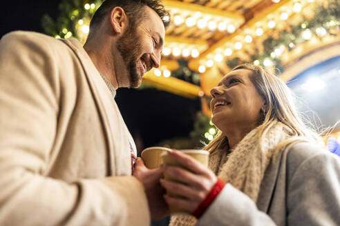 Smiling man and woman enjoying coffee at Christmas market - WPEF07391