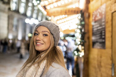 Glückliche junge Frau mit Strickmütze auf dem Weihnachtsmarkt - WPEF07392
