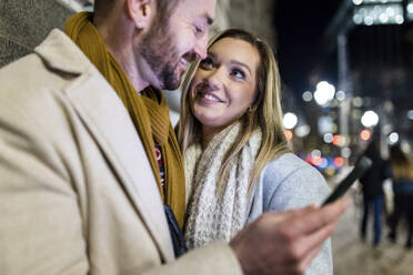 Happy young woman with man holding smart phone - WPEF07395