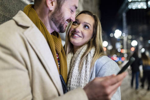 Glückliche junge Frau mit Mann, der ein Smartphone hält - WPEF07395