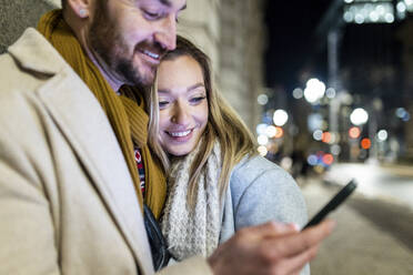 Glückliche junge Frau mit Mann, der ein Smartphone benutzt - WPEF07396