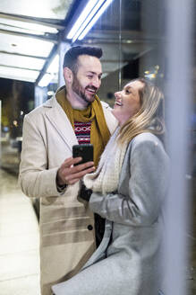 Glücklicher Mann und Frau stehend mit Mobiltelefon - WPEF07400