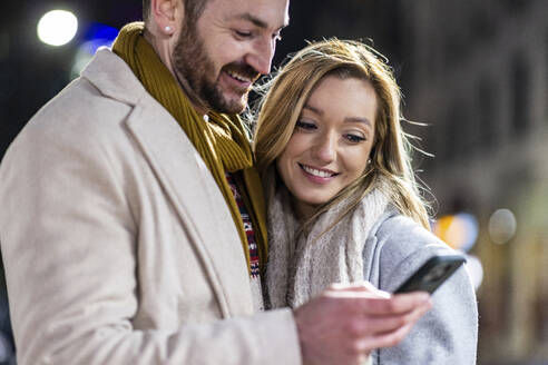 Lächelnder Mann und lächelnde Frau benutzen zusammen ein Mobiltelefon - WPEF07407