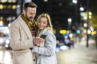 Glücklicher Mann und Frau benutzen Mobiltelefon auf der Straße - WPEF07408