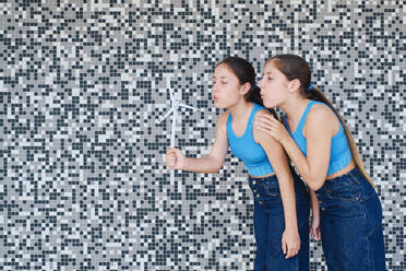 Schwestern, die auf ein Windradmodell vor einer strukturierten Wand blasen - ASGF03598