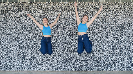 Glückliche Schwestern springen vor einer strukturierten Wand - ASGF03599