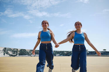 Happy girls holding hands and running in skateboard park - ASGF03608