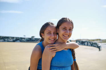 Happy sisters standing on sunny day at skateboard park - ASGF03615
