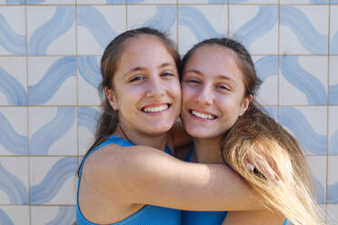 Loving twin sisters hugging in front of wall - ASGF03632