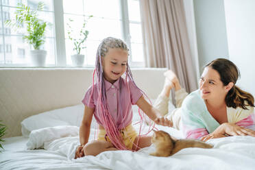 Mutter sieht ihre Tochter an, die mit einem rothaarigen Kätzchen auf dem Bett spielt - MDOF01214