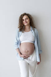 Junge schwangere Frau vor einer Wand stehend - AAZF00643