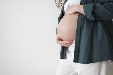 Pregnant woman touching belly in front of wall - AAZF00644