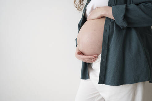 Schwangere Frau, die ihren Bauch vor einer Wand berührt - AAZF00644
