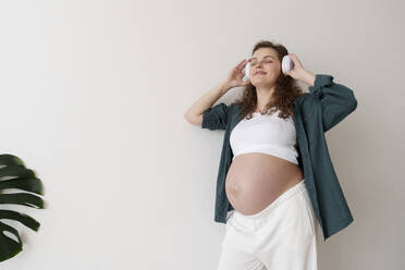 Lächelnde schwangere Frau beim Musikhören - AAZF00647