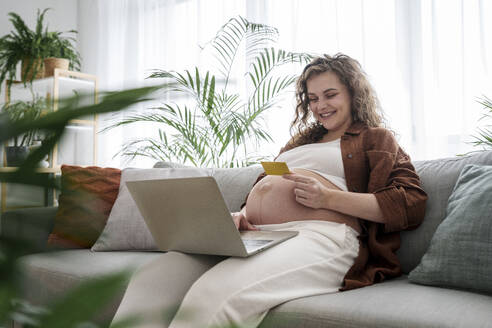 Lächelnde schwangere Frau beim Online-Shopping mit Kreditkarte zu Hause - AAZF00653