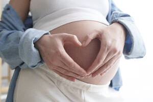Schwangere Frau macht Herzform auf dem Bauch - AAZF00668
