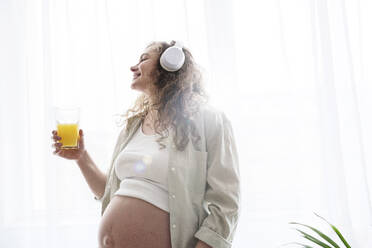 Schwangere Frau trinkt Saft und hört zu Hause Musik - AAZF00671