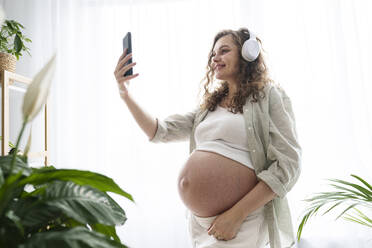 Eine freudige werdende Mutter macht ein Selfie mit ihrem Smartphone, während sie zu Hause ist - AAZF00676