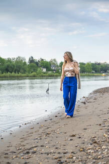 Smiling young woman walking on riverbank - BFRF02426
