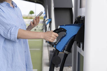 Woman pulling charger from automat at station - EKGF00230