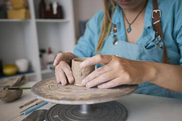 Eine Handwerkerin modelliert eine Tasse aus Ton auf einer Töpferscheibe in einer Werkstatt - ANNF00260