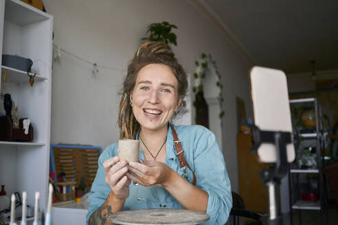 Happy craftswoman holding clay cup at workshop - ANNF00263