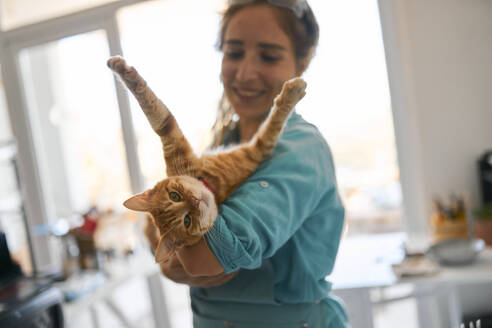 Glückliche Handwerkerin spielt mit Katze in der Werkstatt - ANNF00275