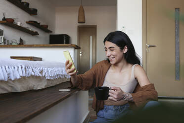 Happy young woman on video call enjoying coffee at home - SYEF00396