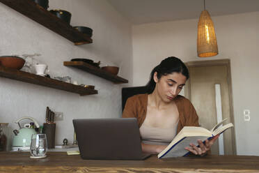 Woman studying with book and laptop on table at home - SYEF00400