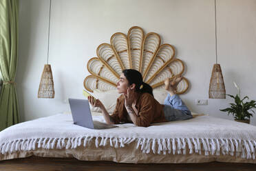 Freelancer liegend mit Laptop und Smartphone auf dem Bett zu Hause - SYEF00401