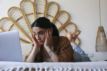 Freiberufler bei der Arbeit mit Laptop auf dem Bett liegend zu Hause - SYEF00402