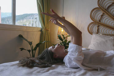 Junge Frau gestikuliert mit den Armen auf dem Bett liegend zu Hause - SYEF00418