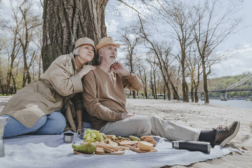 Paar sitzt auf Picknickdecke mit Snacks am Strand - YTF00893