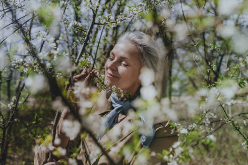 Reife Frau mit geschlossenen Augen riecht an Blumen im Wald - YTF00899