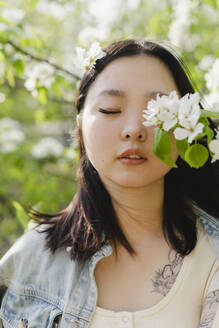 Junge Frau mit geschlossenen Augen bei weißen Blumen auf einem Zweig - SEAF01951