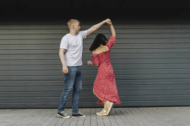 Junges Paar tanzt vor einem geschlossenen Fensterladen - SEAF01958