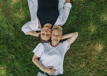Lesbian couple with hands behind head lying on grass - VSNF01017