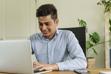 Lächelnder Geschäftsmann mit Laptop am Schreibtisch im Büro - OSF01599