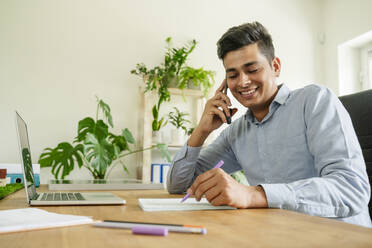 Smiling businessman talking on smart phone in office - OSF01609