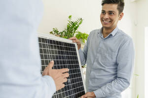 Ein lächelnder Geschäftsmann zeigt einem Kollegen im Büro ein Solarmodul - OSF01621