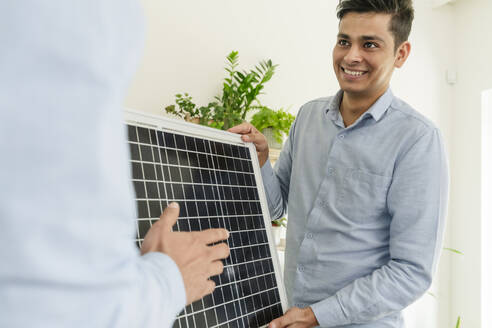 Smiling businessman showing solar panel to colleague in office - OSF01621