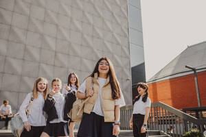 Glückliches Mädchen, das sich mit Freunden vor einem Schulgebäude amüsiert - MDOF01268